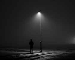 Man standing in the dark under a street lamp listening to silence
